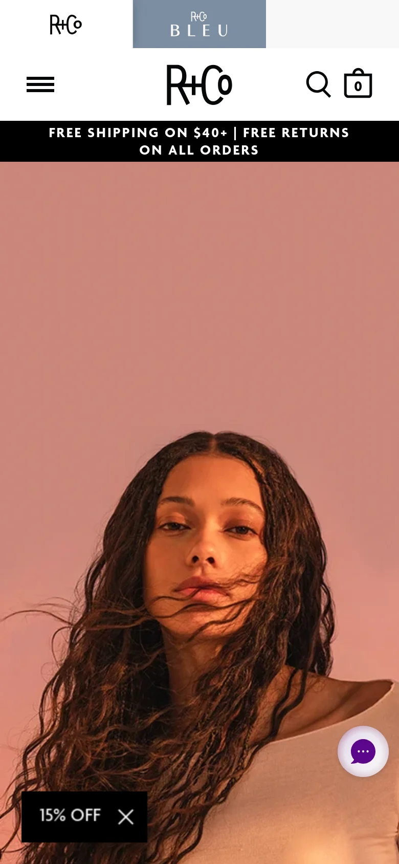 The mobile version displays a vertically oriented hero image of a woman with wavy hair against a pink background. The header is condensed with a hamburger menu icon, the R+Co logo, a search icon, and a shopping bag icon. A promotional '15% OFF' overlay is visible in the bottom left corner.