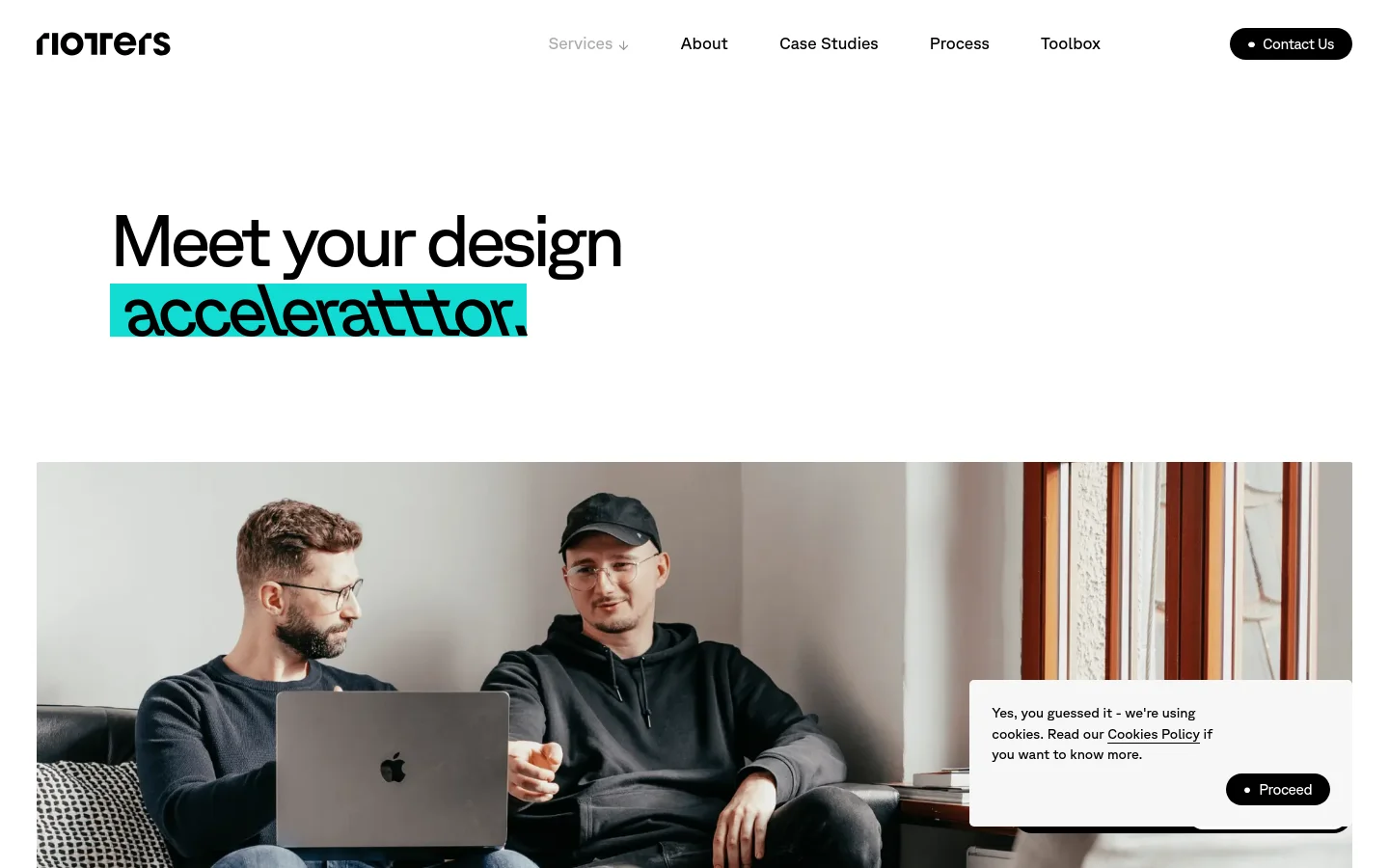 The desktop version features a clean white background with the headline 'Meet your design acceleratttor.' in large black text, with 'acceleratttor' highlighted in bright teal. Below the headline is a large hero image of two men working on a laptop in a modern indoor setting. A navigation bar at the top includes links for Services, About, Case Studies, Process, and Toolbox, alongside a black 'Contact Us' button.