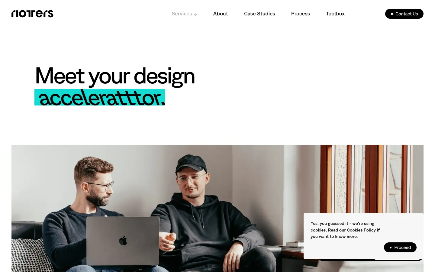 The desktop version features a clean white background with the headline 'Meet your design acceleratttor.' in large black text, with 'acceleratttor' highlighted in bright teal. Below the headline is a large hero image of two men working on a laptop in a modern indoor setting. A navigation bar at the top includes links for Services, About, Case Studies, Process, and Toolbox, alongside a black 'Contact Us' button.