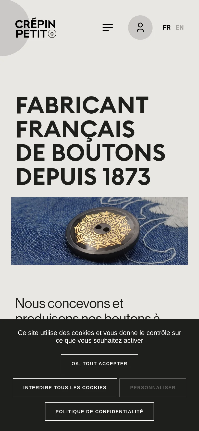 The mobile version presents a vertically stacked layout with the large bold headline at the top, followed by the hero image of the decorative button. The navigation is condensed into a hamburger menu icon next to a user profile icon, and a cookie consent banner occupies the bottom of the screen.