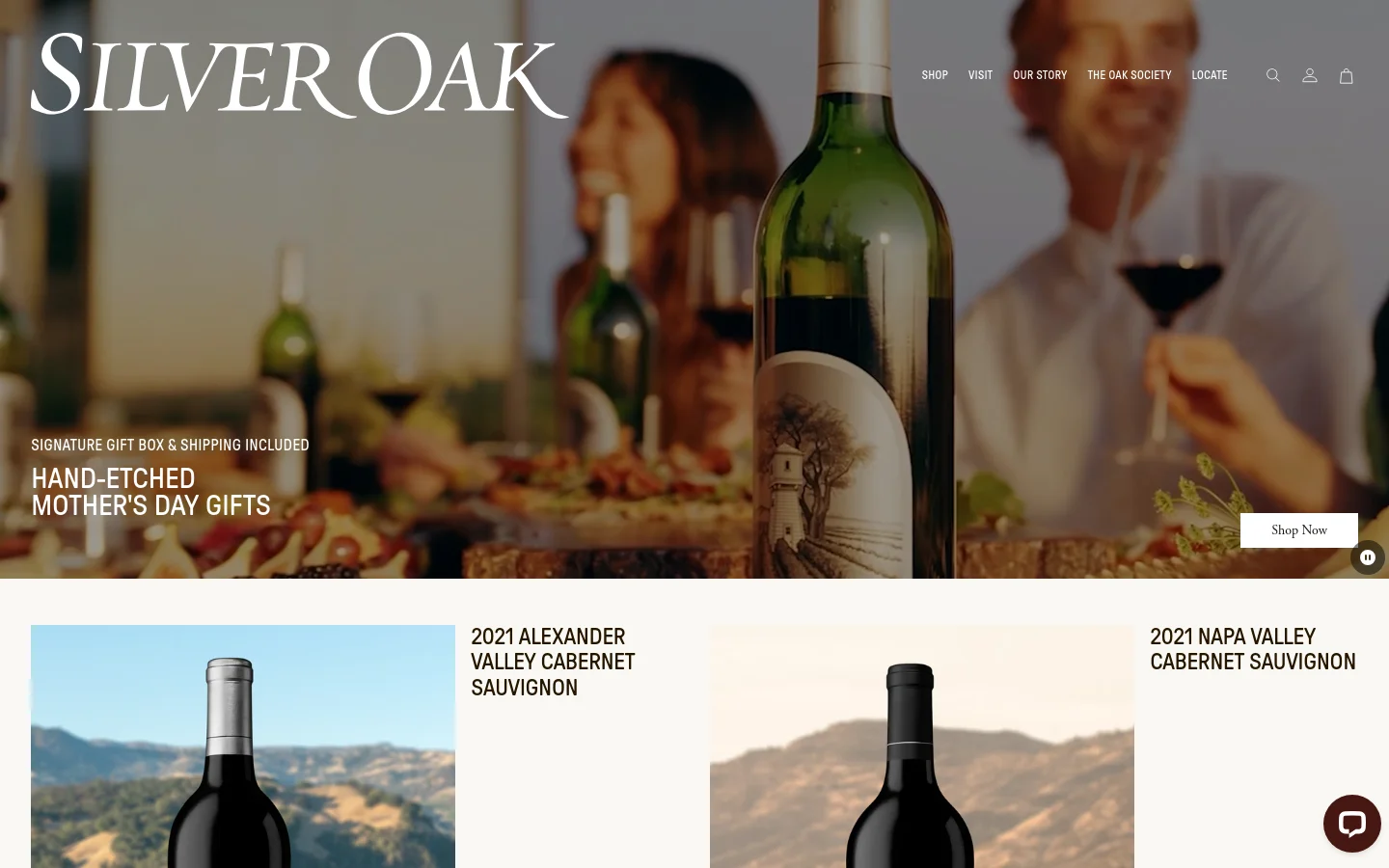 The desktop homepage features a large hero image of people enjoying wine in a warm, blurred setting, with a headline for hand-etched Mother's Day gifts and a 'Shop Now' button. Below, a grid layout showcases 2021 Alexander Valley and Napa Valley Cabernet Sauvignon bottles against scenic vineyard landscapes. The design uses elegant serif typography and a sophisticated color palette of deep greens, earthy tones, and white.