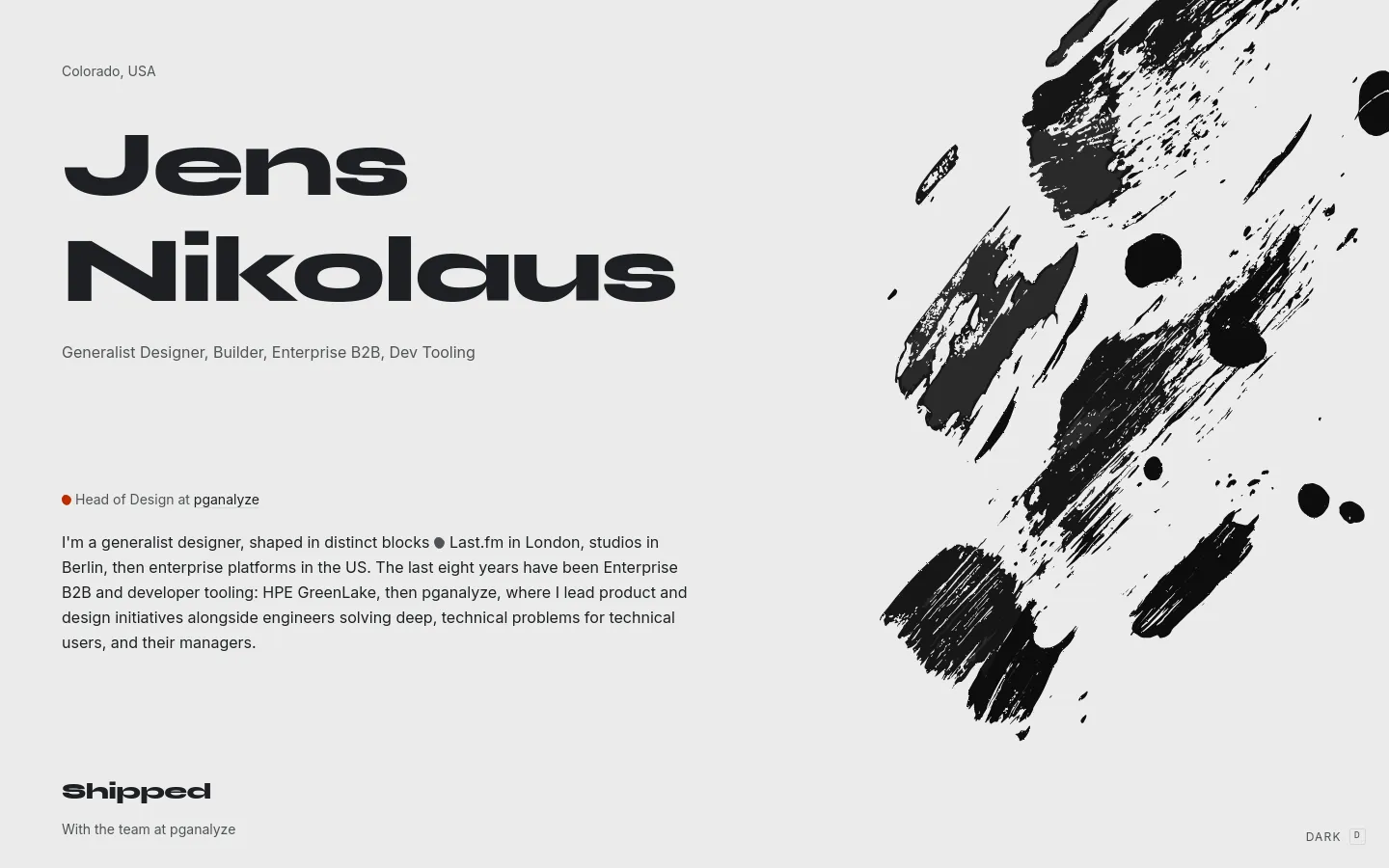 A minimalist personal website with a light gray background and bold black typography. The headline 'Jens Nikolaus' is prominently displayed on the left, accompanied by a large, expressive black ink brushstroke graphic on the right. The layout features a clean, single-column text structure with sections for professional bio and 'Shipped' projects.