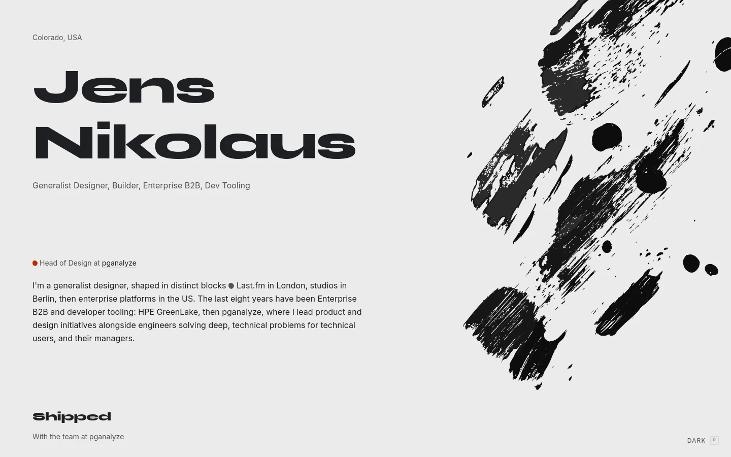 A minimalist personal website with a light gray background and bold black typography. The headline 'Jens Nikolaus' is prominently displayed on the left, accompanied by a large, expressive black ink brushstroke graphic on the right. The layout features a clean, single-column text structure with sections for professional bio and 'Shipped' projects.