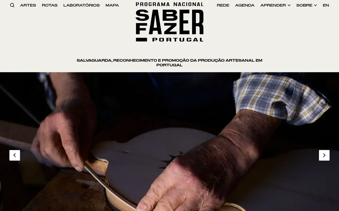 The desktop homepage features a clean, white header with the 'Saber Fazer Portugal' logo centered and a navigation menu spread across the top. Below, a large hero carousel displays high-quality images of traditional craftsmanship, such as hands working on a musical instrument, with navigation arrows on the sides. The page uses a minimalist aesthetic with bold black typography and clear calls to action like 'Explore o Atlas'.