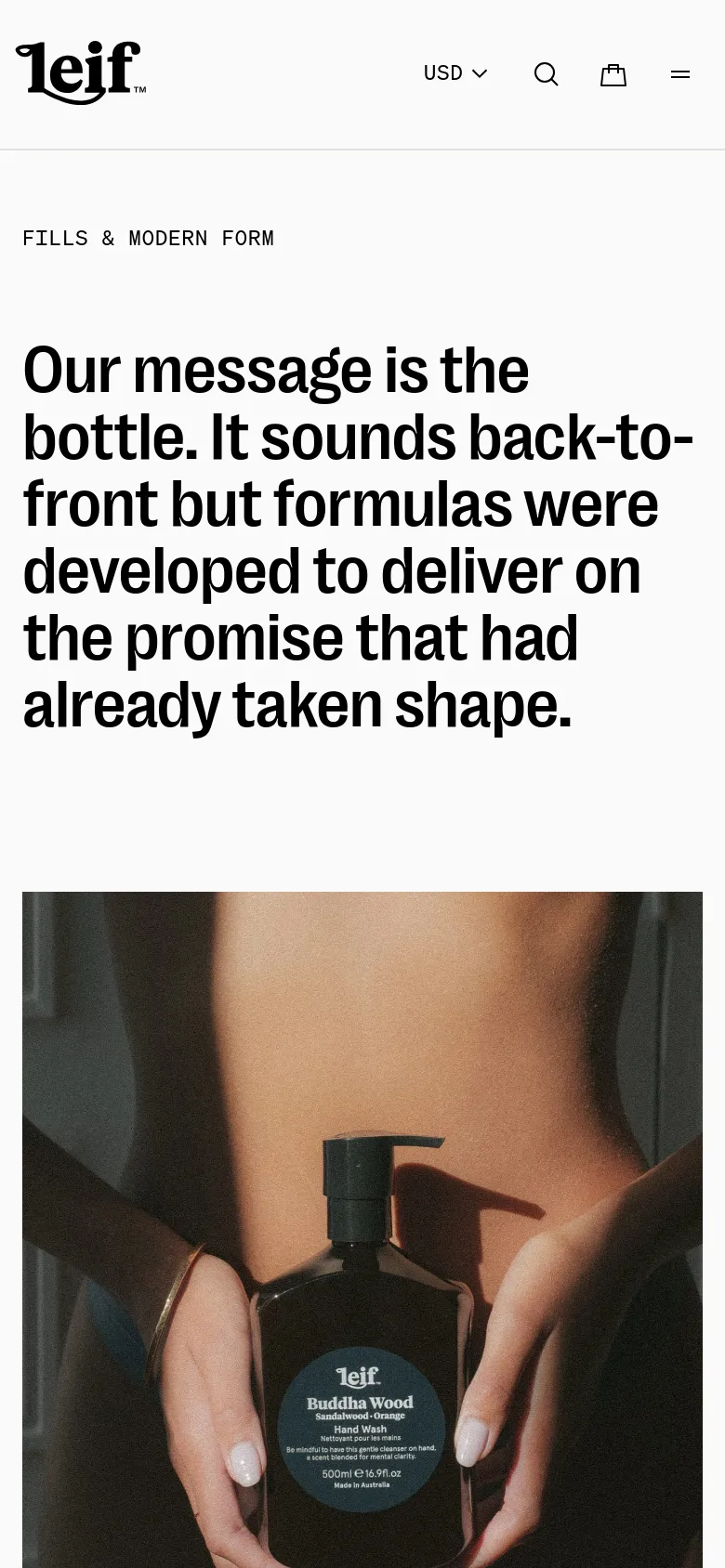 The mobile version uses a single-column vertical layout, stacking the large headline text above the hero image of the hand wash bottle. The top navigation is condensed into a hamburger menu icon next to the brand logo, and the currency selector and search icon are centered.