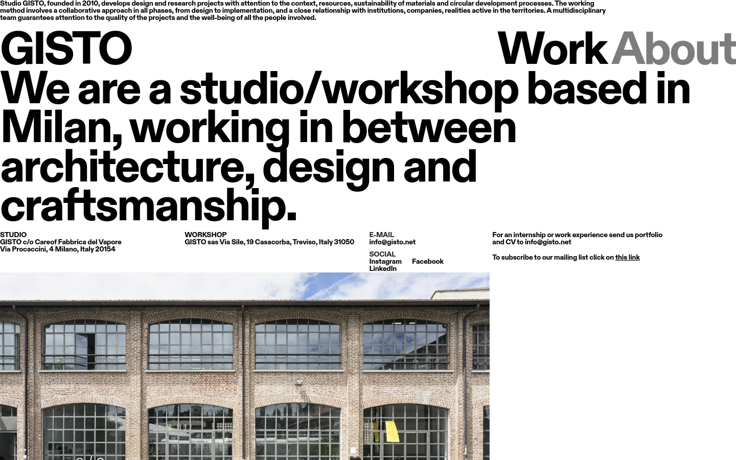 The desktop page features a minimalist white layout with large, bold black typography. A massive headline introduces the studio, followed by contact details for the Milan studio and Treviso workshop arranged in columns, alongside social media links and a call to action for internships. A wide landscape photograph of a brick building with large industrial windows sits at the bottom of the viewable area.