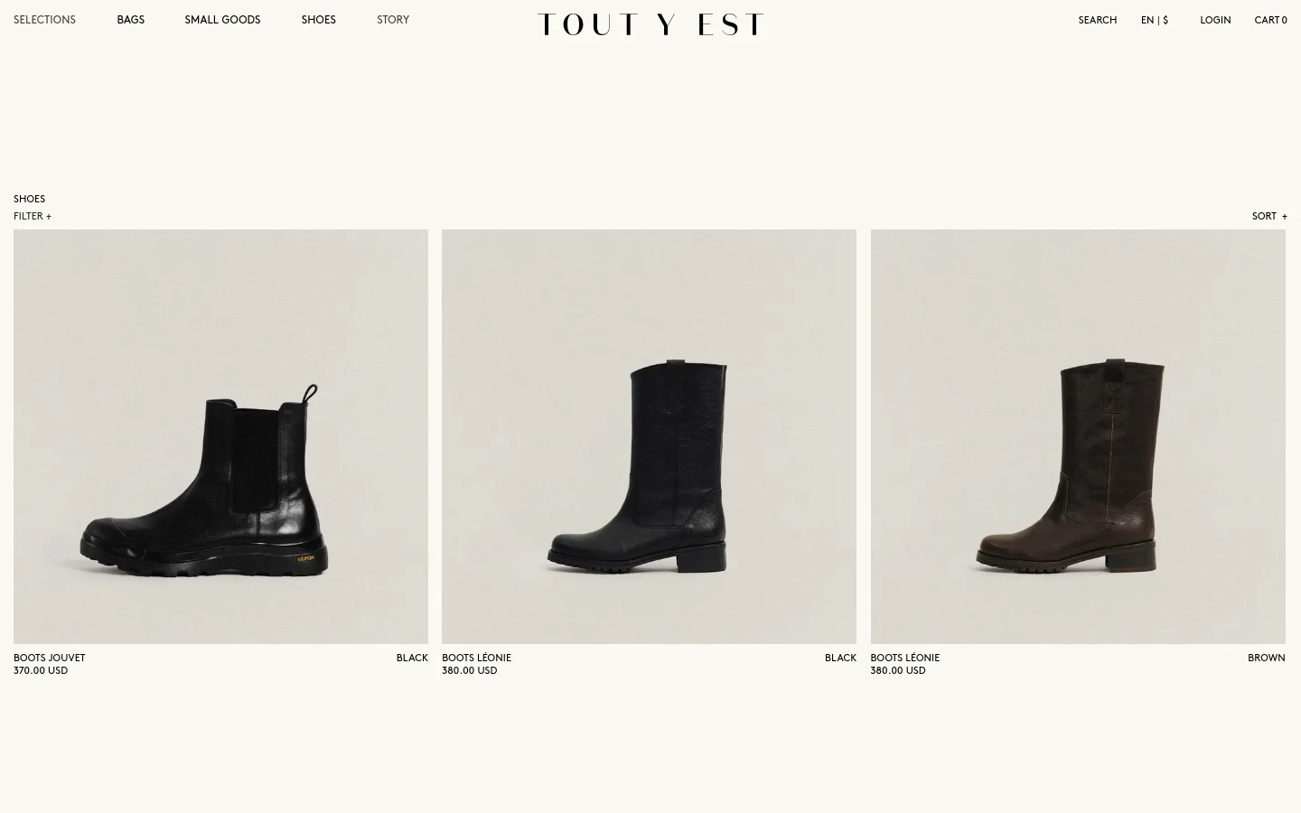 The desktop version of the Shoes collection page features a minimalist design with a white background and black serif typography. A navigation bar at the top includes links for Bags, Small Goods, Shoes, and Story, alongside a central brand logo. The main content displays a grid of product images showing various black and brown leather boots, with product names and prices listed below each item.