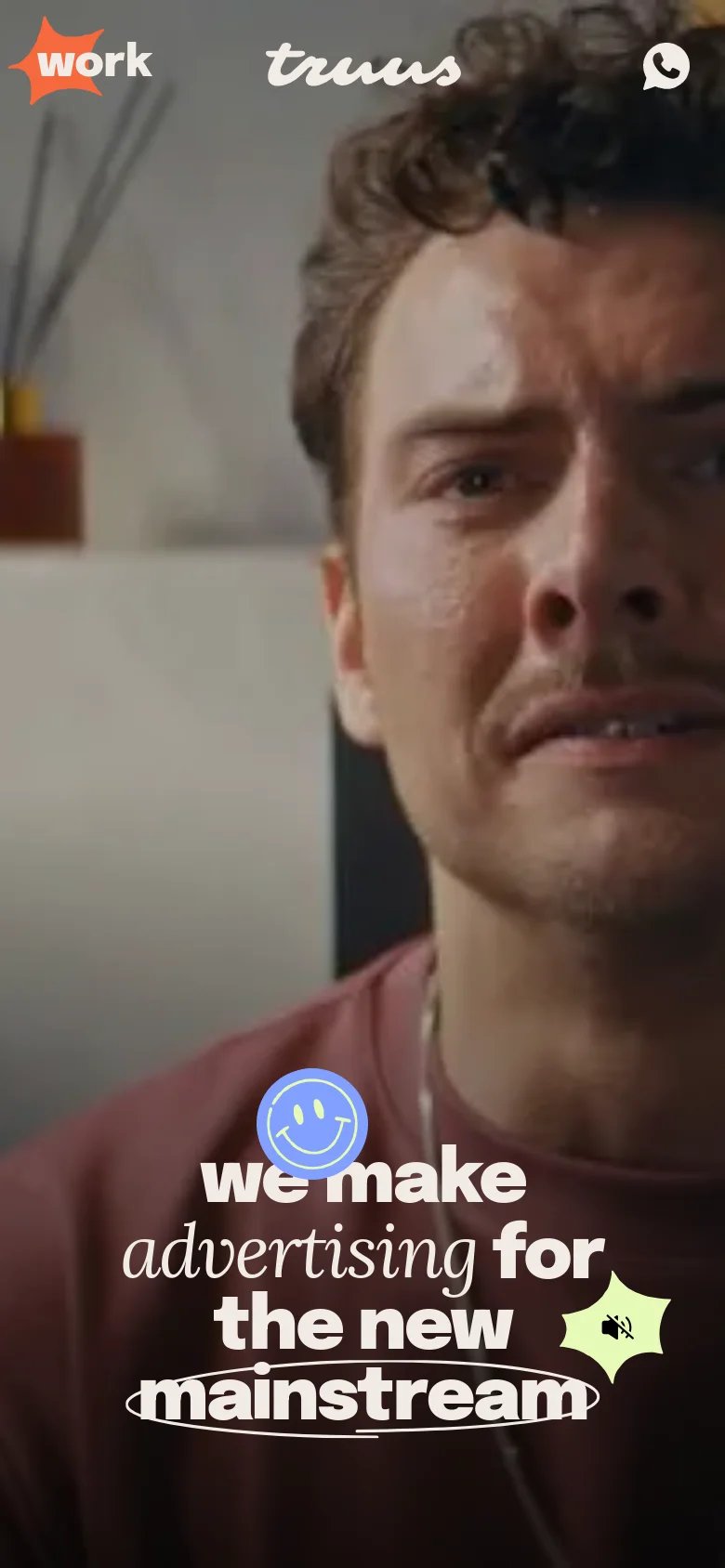 The mobile version presents a vertically cropped version of the hero video, focusing closely on the man's face. The bold white headline 'we make advertising for the new mainstream' is centered over the video, and the navigation elements are condensed to fit the narrow screen width.