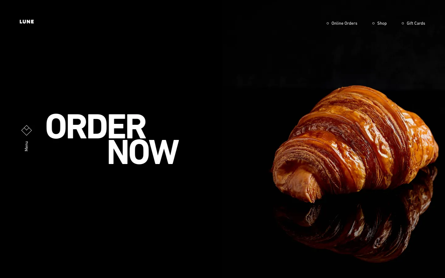 The desktop homepage features a minimalist dark design with a large, high-resolution hero image of a golden-brown croissant on a reflective black surface. Large white text reads 'ORDER NOW' prominently on the left, with the Lune logo in the top left and navigation links for Online Orders, Shop, and Gift Cards in the top right.