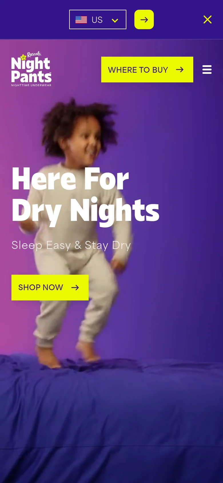 The mobile version uses a vertical layout with a blurred background image of a child jumping on a bed. The 'Here For Dry Nights' headline and 'SHOP NOW' button are centered, while the navigation is condensed into a hamburger menu icon next to a yellow 'WHERE TO BUY' button.