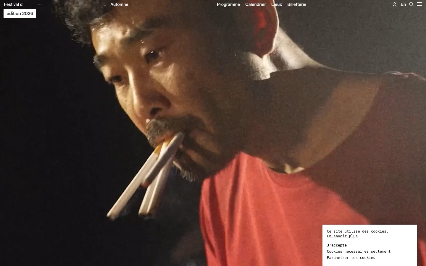 The homepage for Festival d'Automne features a large, full-screen hero image of a performer in a red shirt. A white navigation bar at the top contains the festival logo, links for Programme, Calendrier, Lieux, and Billetterie, and a language selector. The color palette is dark and cinematic, dominated by the high-contrast photography.