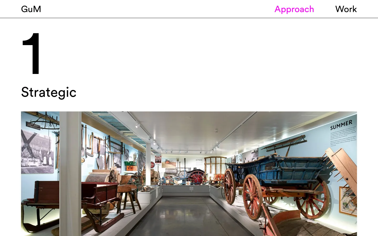 The desktop page features a clean, minimalist white background with large black typography. A large number '1' sits above the headline 'Strategic', followed by a wide landscape photograph of a museum interior showcasing historical agricultural tools and a blue wooden cart. Below the image, text describes the company's strategic approach, citing the Museum of English Rural Life as an example.