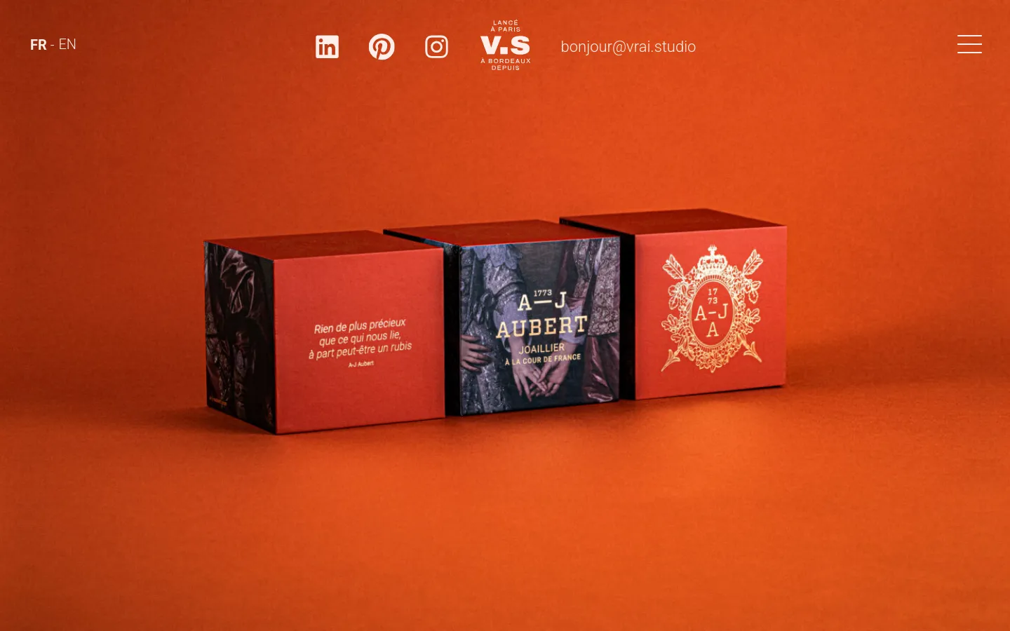 Desktop view of a luxury branding project page featuring a large hero image of red jewelry boxes with gold emblems against a burnt orange background. The navigation bar includes language selection, social media icons, the studio logo, an email contact, and a hamburger menu.