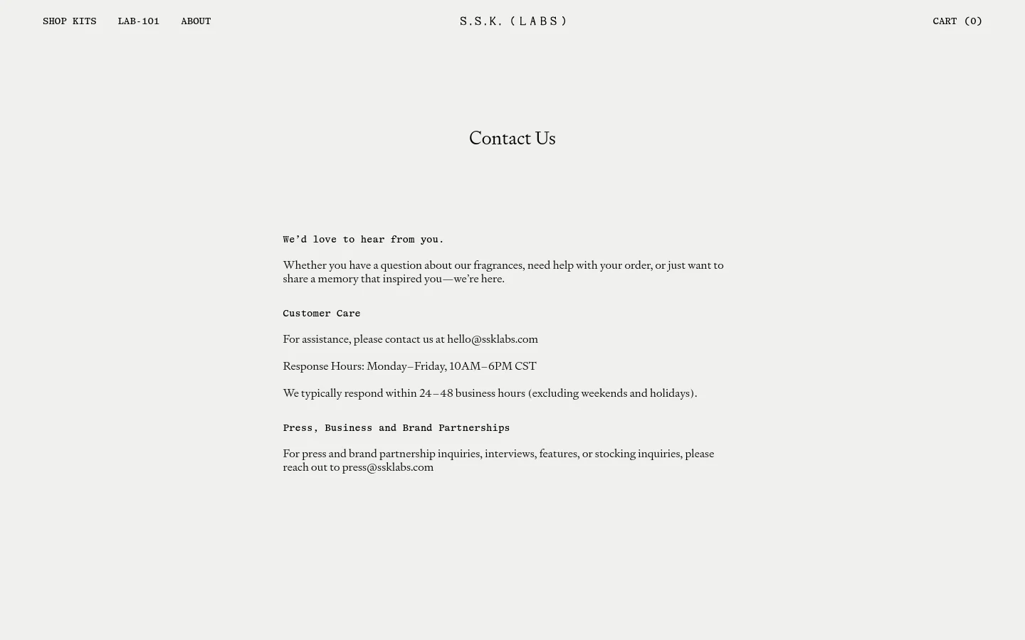 The desktop Contact Us page features a minimalist design with a light beige background and black serif typography. The layout is centered, displaying the 'Contact Us' headline followed by sections for customer care and business partnerships with their respective email addresses. The navigation bar at the top includes links for Shop Kits, Lab-101, and About, alongside the brand name and a cart icon.