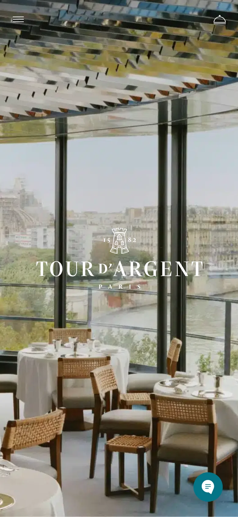 The mobile version presents a vertically oriented view of the same elegant restaurant interior and cityscape. The navigation is condensed into a hamburger menu icon at the top left, and a floating chat bubble icon is visible at the bottom right for customer inquiries.