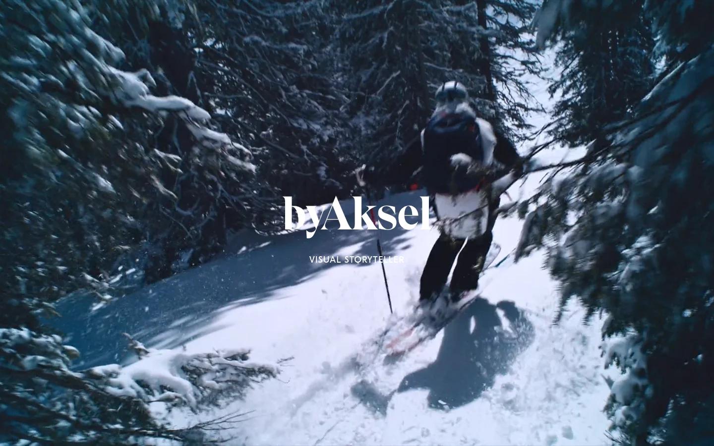The desktop homepage features a full-screen, cinematic hero image of a person skiing through a snowy forest, with the brand name 'byAksel' and the headline 'VISUAL STORYTELLER' centered in white text. The layout is minimalist, dominated by the high-contrast blue and white tones of the winter landscape.