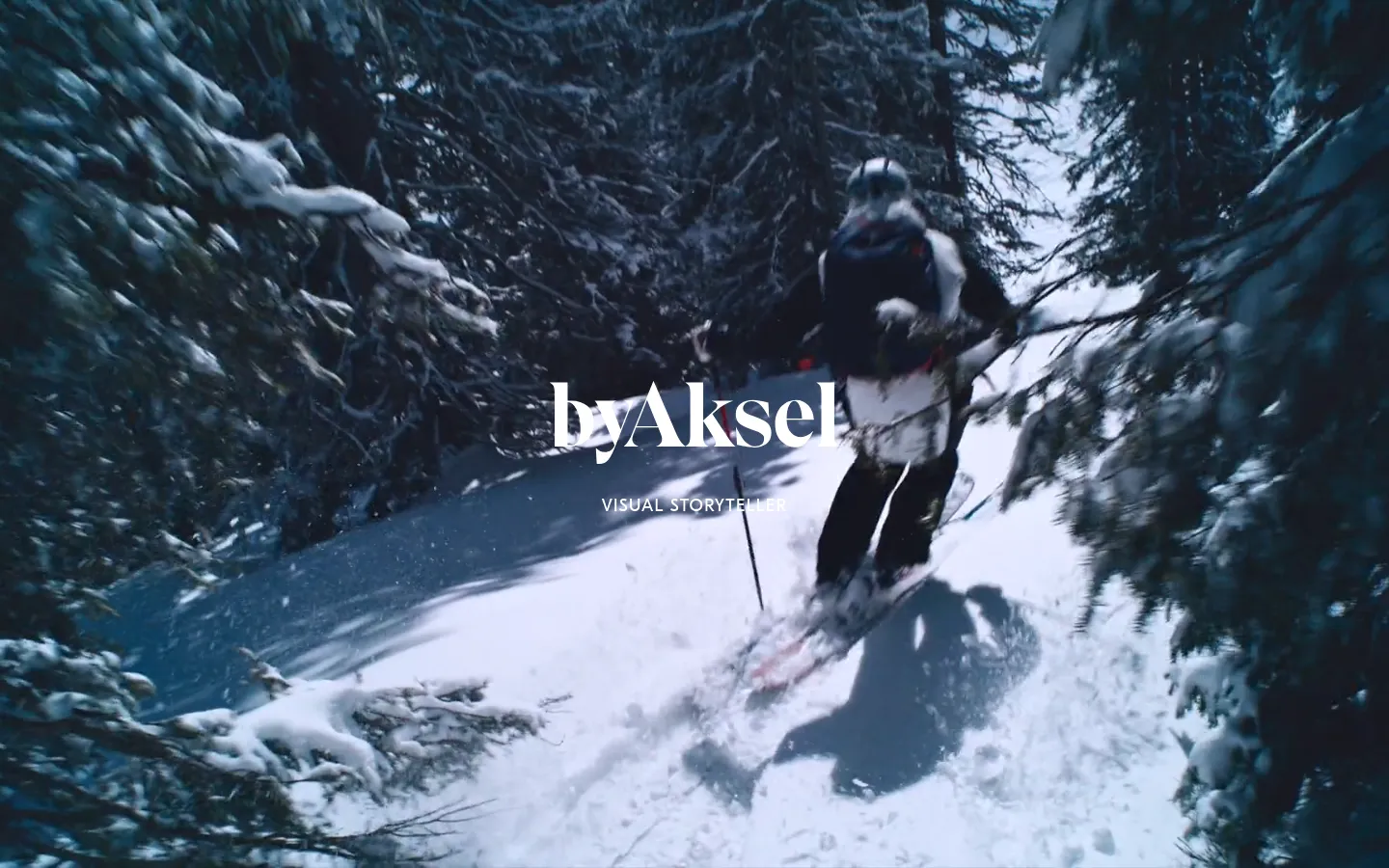 The desktop homepage features a full-screen, cinematic hero image of a person skiing through a snowy forest, with the brand name 'byAksel' and the headline 'VISUAL STORYTELLER' centered in white text. The layout is minimalist, dominated by the high-contrast blue and white tones of the winter landscape.