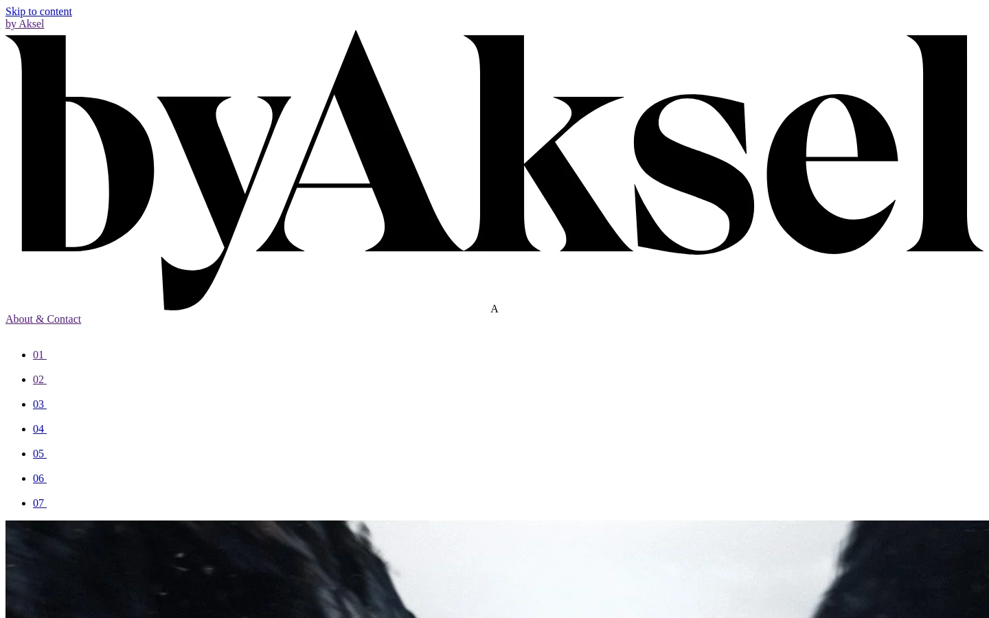 The desktop page features a minimalist white background with large, black serif typography for the 'byAksel' logo and navigation. A vertical list of numbers (01-07) serves as the main navigation, with '02' highlighted to indicate the current page. Below the header, a large, cinematic landscape image shows a dark, rocky coastal scene under a bright sky.