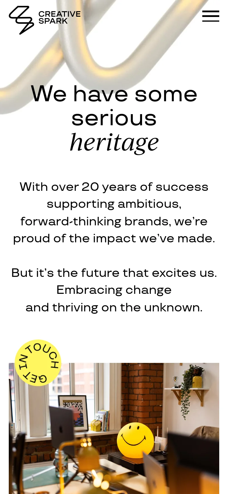 The mobile version maintains the minimalist aesthetic but uses a stacked vertical layout optimized for smaller screens. The hero headline and text are centered, and the top navigation is replaced by a hamburger menu icon on the right. The 'Get in Touch' circular button is prominently positioned over a lifestyle image of a workspace.