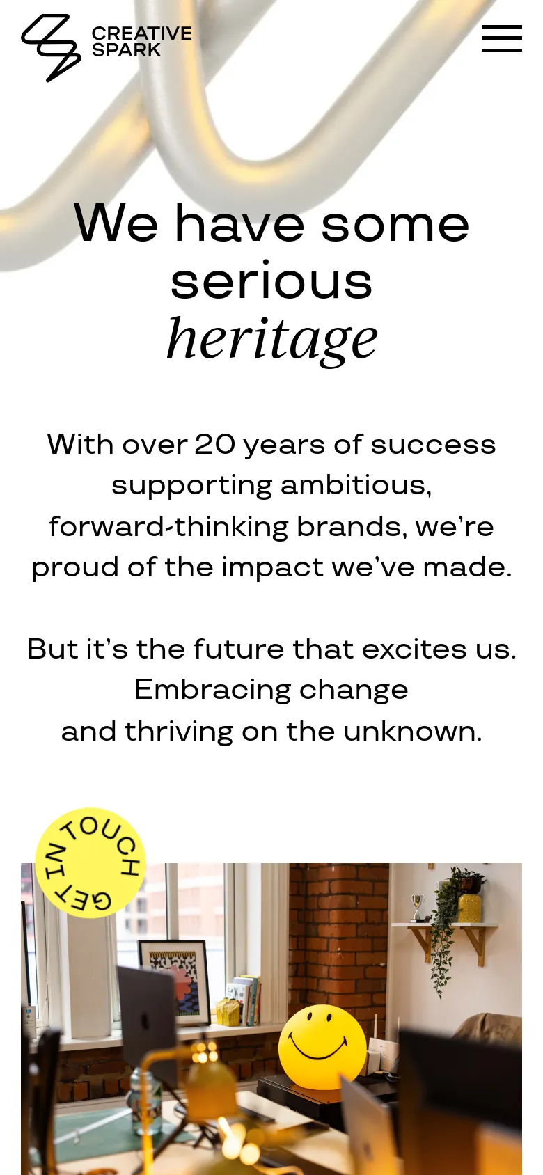 The mobile version maintains the minimalist aesthetic but uses a stacked vertical layout optimized for smaller screens. The hero headline and text are centered, and the top navigation is replaced by a hamburger menu icon on the right. The 'Get in Touch' circular button is prominently positioned over a lifestyle image of a workspace.