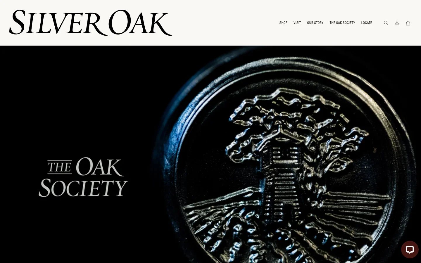 The desktop landing page for The Oak Society features a large, dark hero image of a metallic seal embossed with an oak tree. The Silver Oak logo is at the top left, with navigation links and account icons on the right. The layout transitions into a clean white section with elegant serif typography, explaining the loyalty program and providing 'Create Your Account' and 'Start a Subscription' call-to-action buttons.