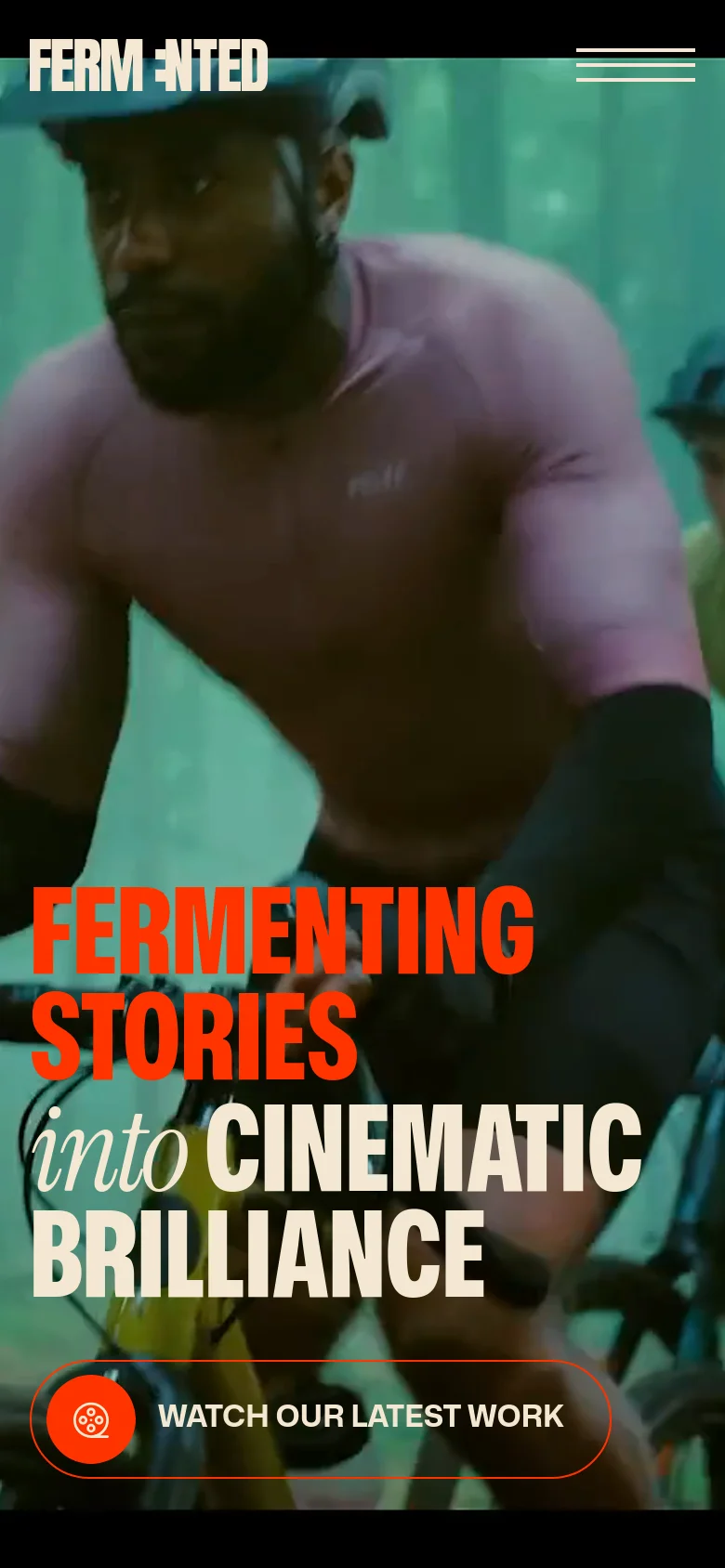 The mobile version presents a vertically oriented view of the hero video, focusing closely on a cyclist. The large red and white headline and the 'WATCH OUR LATEST WORK' call-to-action button are centered and scaled for a smaller screen. The navigation is condensed into a hamburger menu icon in the top right corner.