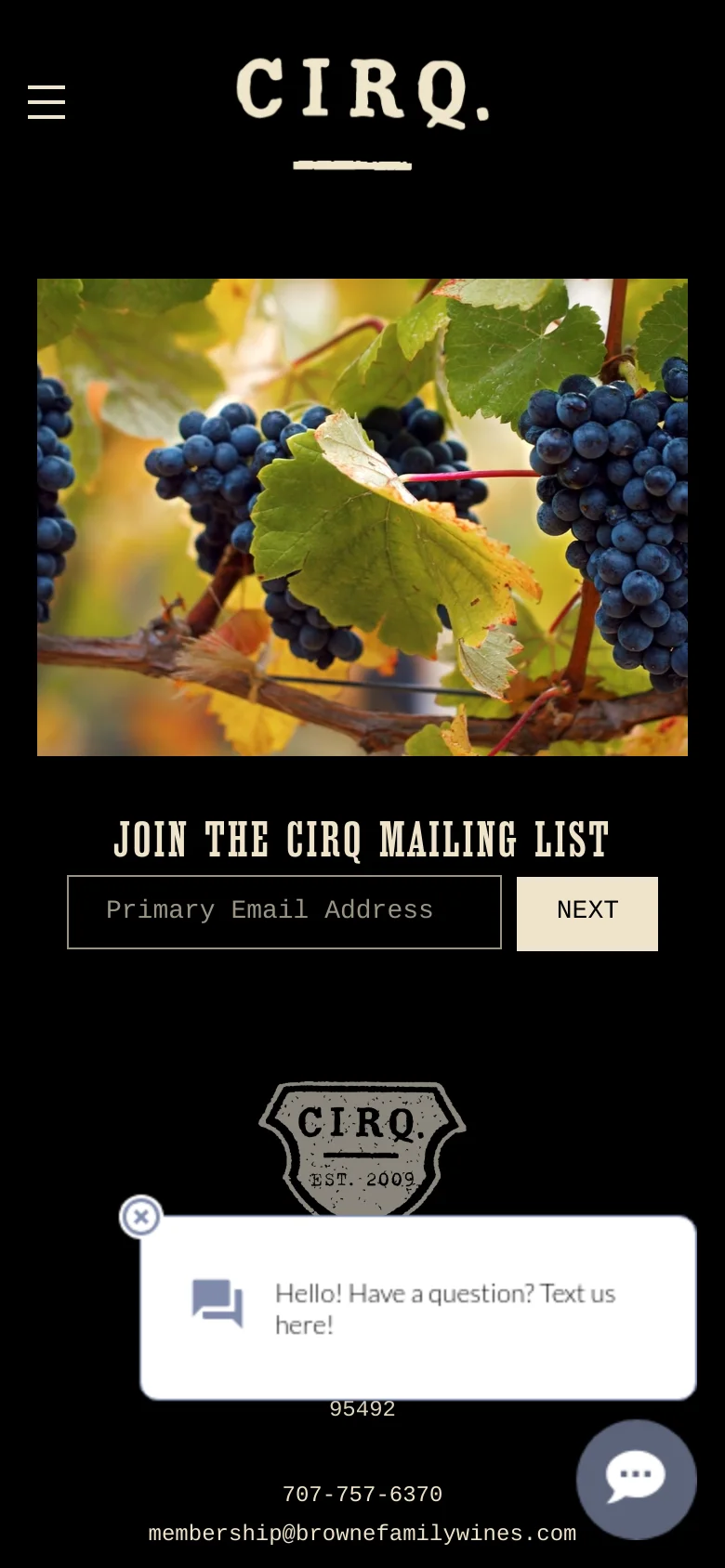 The mobile version maintains the dark theme but simplifies the layout, centering the 'CIRQ.' logo at the top. The hero image is replaced by a close-up of dark purple grapes on a vine, with the mailing list signup form positioned directly below it. A chat widget is visible in the bottom right corner.