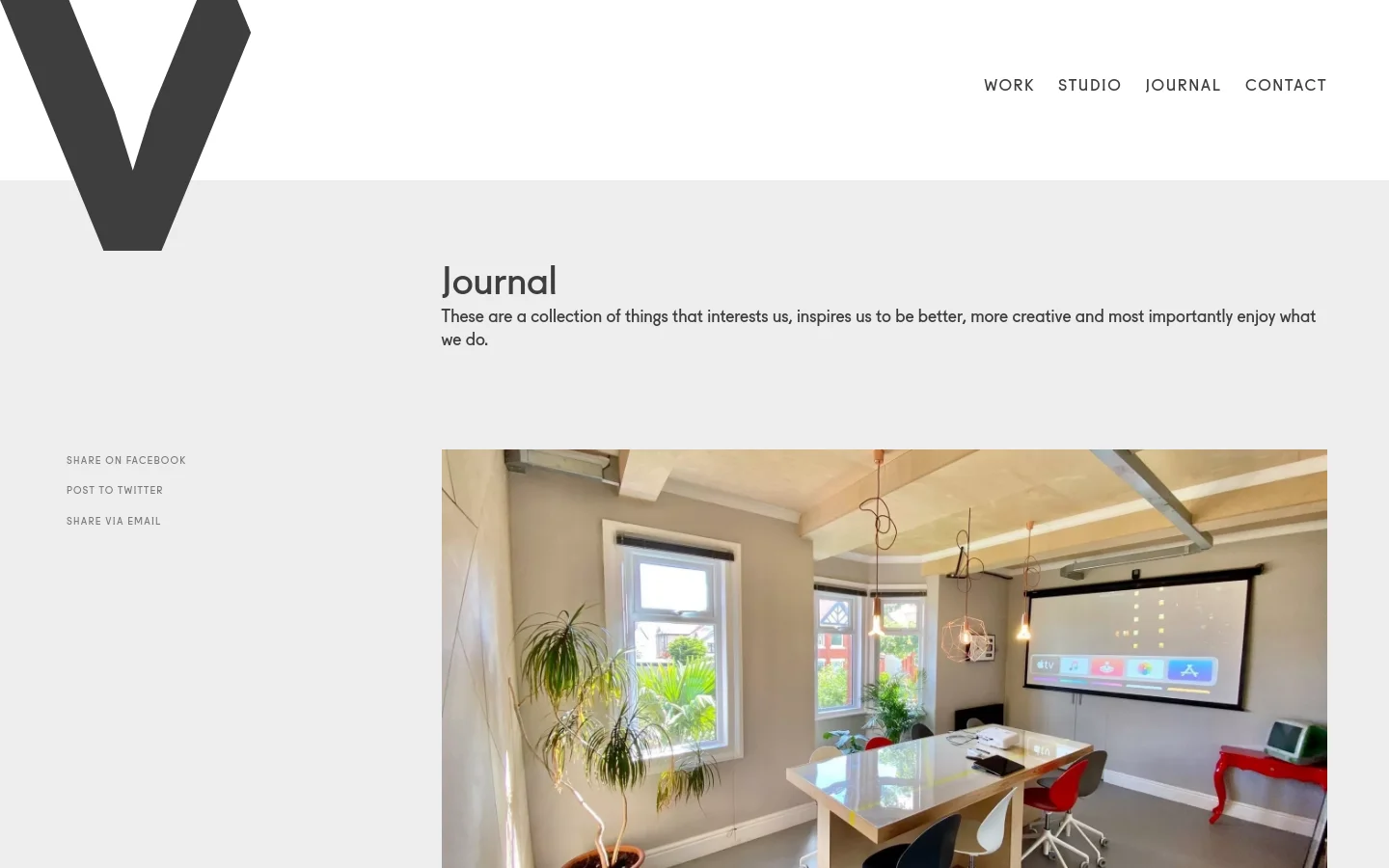 The Journal page features a minimalist design with a large dark 'V' logo on the left and a clean navigation menu on the right. A light gray header contains the title 'Journal' and a brief introductory paragraph, followed by social sharing links and a large photograph of a bright, modern creative studio space with a desk and projector screen.