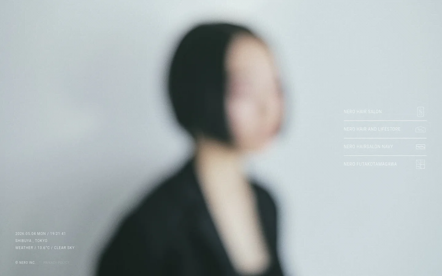 A minimalist desktop homepage featuring a large, soft-focus portrait of a person against a light gray background. On the right side, four text-based navigation links for different salon brands are vertically aligned, and the bottom left displays the date, location, and weather in small white text.