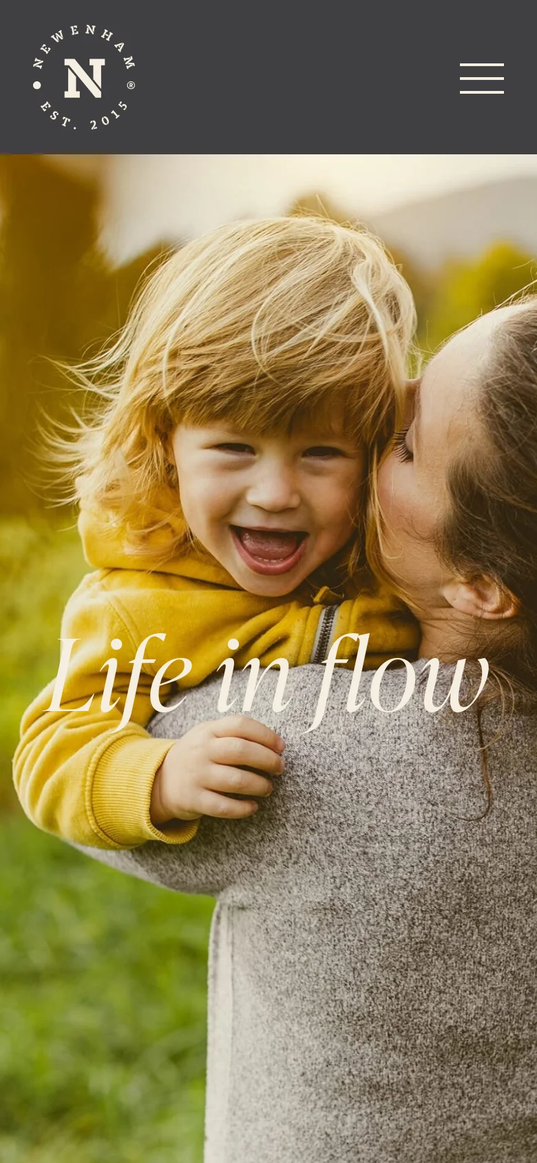 The mobile version simplifies the layout with a dark grey header containing the Newenham logo and a white hamburger menu icon on the right. The hero image of a woman holding a laughing child remains the central focus, with the 'Life in flow' text overlaid prominently.