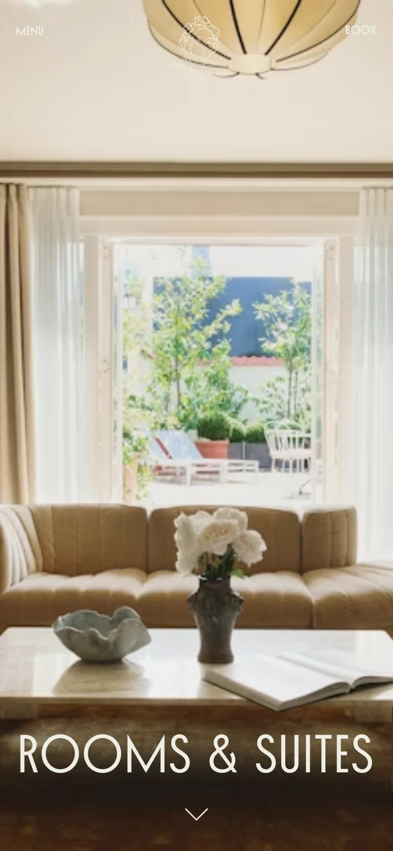 The mobile version presents a vertically oriented version of the hero image, focusing on the central lounge area and the view through the open balcony doors. The 'ROOMS & SUITES' headline and navigation links remain visible, but the composition is tighter to fit the narrow screen. The overall aesthetic maintains the bright, airy, and high-end feel of the desktop view.